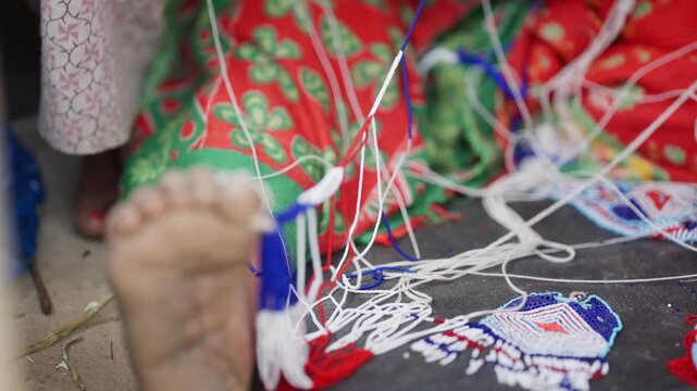 Bare foot anchoring loose pote bead thread strands against vivid red and green floral traditional fabric in far west Nepali handicraft scene