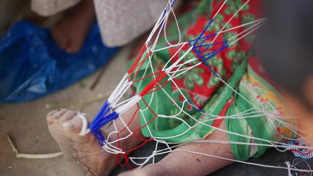 Bare foot anchoring handmade pote bead thread setup with red and white strands stretched across traditional green and red fabric background