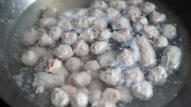 Fresh raw meatballs simmering gently in a pot of boiling water, steam rising, close-up shot capturing texture and cooking process for culinary or food preparation content.