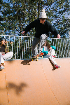 Skateboarder perform trick at outdoor ramp with friends