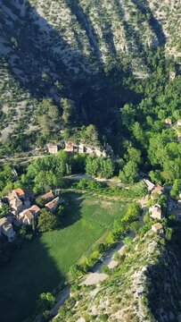 Vertical 9:16 aerial video of the village of Navacelles nestled in a lush green valley surrounded by steep rocky hillsides.