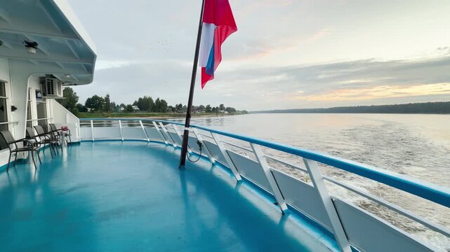 A cruise ship sails calmly along the Neva River, flying a flag on the open deck. The serene waterway view brings a feeling of happy tranquility and peace.
