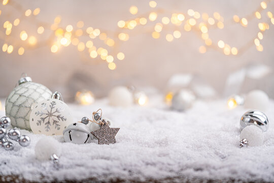 Elegant silver and white ornaments, stars, and bells lie on snow with glowing lights in the background, creating a calm and festive winter holiday setting. Ideal for holiday greeting cards,