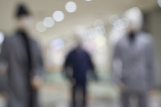 Mannequins And Blurred Shoppers Standing In Indoor Shopping Mall Corridor With Overhead Bokeh Lights Shallow Depth Of Field Soft Focus.