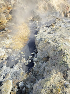 Close view of a steaming fumarole surrounded by yellow sulphur deposits and altered rock in a geothermal field in Iceland.