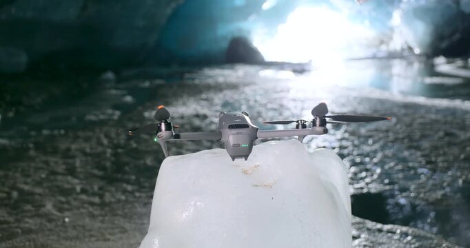 Camera drone resting on an ice block inside a frozen cave, propellers ready under dramatic backlight