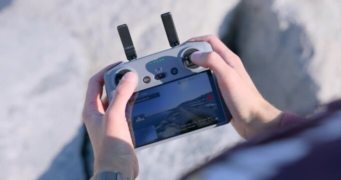 Close-up of hands operating a drone controller with built-in screen outdoors, adjusting flight controls and viewing live camera feed