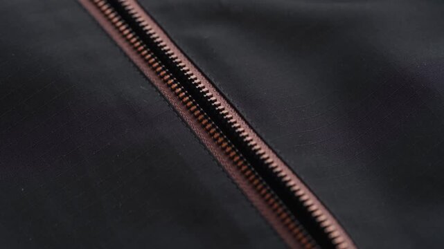 A close-up shot of a hand unzipping a black waterproof jacket with brown zipper details.