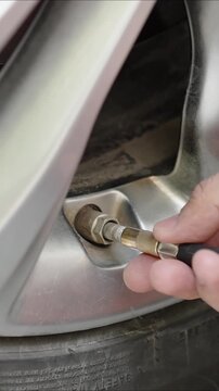 Vertical video of detailed close-up of driver hand attaching air hose to car tire valve on alloy wheel. Routine tire pressure maintenance, road safety and vehicle care.