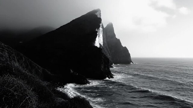 Dramatic black and white ocean coastline showcasing imposing cliffs with dark foreboding mood and atmospheric light