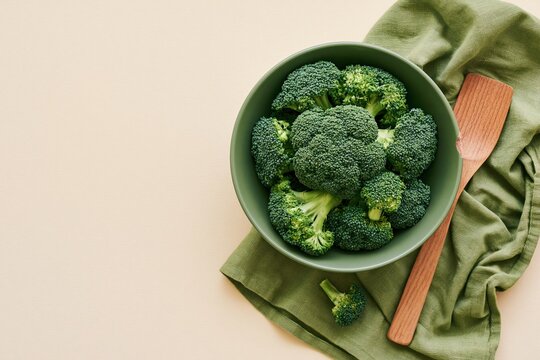 Ceramic bowl of fresh broccoli florets on a crumpled cloth with a wooden utensil, featuring natural textures and copy space for healthy eating campaigns