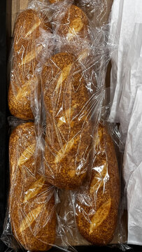 A vertical display of packaged fresh baguettes, generously coated with sesame seeds, in the bakery aisle.