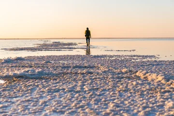 Man traveler with backpack walking on the salt lake at sunrise. Salt crystals surface with water. Baskunchak lake, Russia © smallredgirl