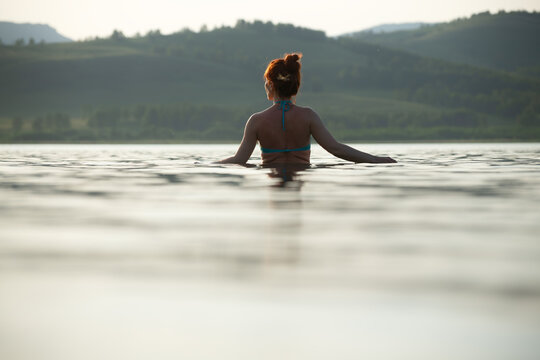 Woman swims in the lake at sunset and enjoying the view of the mountains. Concept of a healthy lifestyle and relaxation in nature