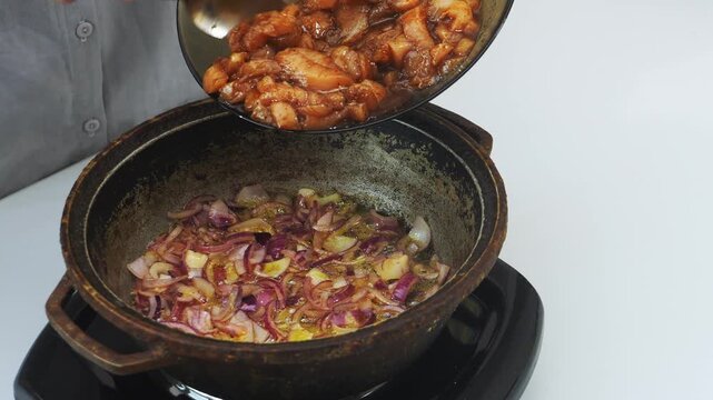 In a deep cast-iron skillet, onions are fried in vegetable oil with chicken marinated