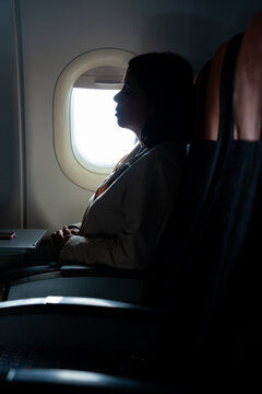 Woman passenger sleeping by airplane window during flight, experiencing jet lag and exhaustion, finding solitude in travel