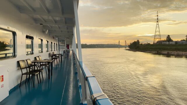 A cruise ship sails calmly along the Neva River at sunset. The golden light reflects off the water and open deck. The serene journey brings a feeling of happy tranquility.