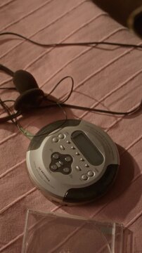 Vertical shot of vintage portable CD player with headphones resting on pink fabric. Clip is ideal for retro technology reviews, 90s nostalgia content, or music history documentaries