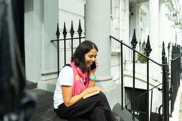 Fototapeta premium Woman making phone call sitting on steps in London, enjoying conversation and urban connectivity