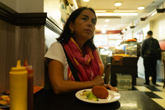 Woman having a casual meal, sitting at a table in a city snack bar, enjoying a peaceful moment while dining out