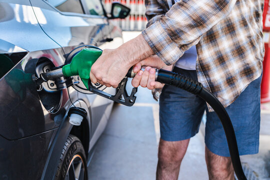 Man refueling passenger car at gas station with green fuel nozzle