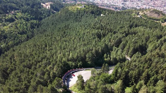 Drone Aerial View Flying Over Dense Trebevic Forest Revealing Winding Mountain Road and City Landscape