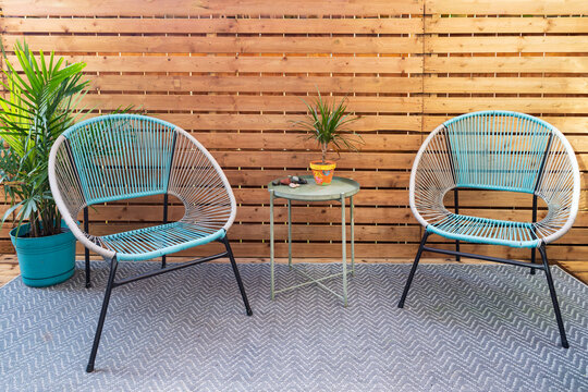 Modern home terrace with wooden slate screen, exterior carpet, retro style grey and turquoise chairs, small round metal table and plants 