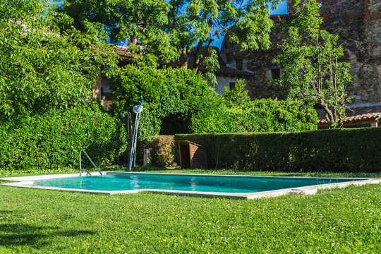 Swimming pool beside restored Mediterranean stone farmhouse surrounded by lush garden and mature trees