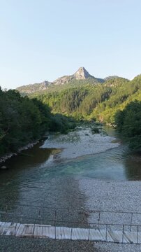 Drone Aerial View Flying Over Wooden Footbridge Towards Shallow Neretva River and Mountain Peak in Glavaticevo