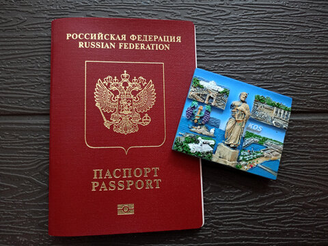 Moscow, Russia - 07.22.2026: A Russian passport with a magnet featuring views of the Greek island of Kos on a dark background. Concept for travel to Greece, tourist trip - horizontal photo, close-up