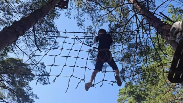 Child climbs a rope net under trees at a summer camp in the afternoon