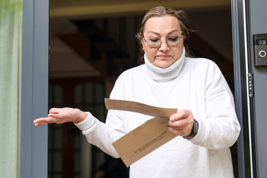 Older woman looking upset and confused while holding a brown envelope with an official letter, illustrating financial stress, unexpected expenses and financial problems.