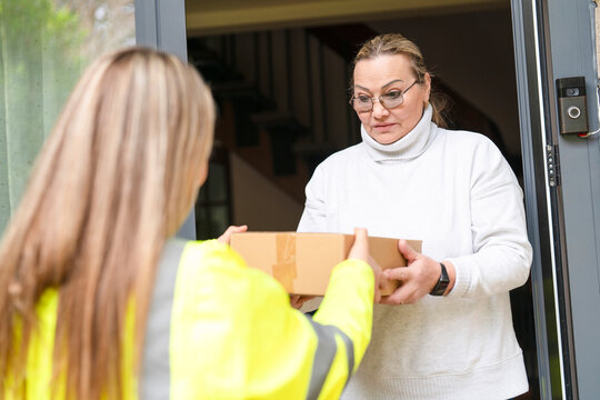 Delivery person hands a package to a woman at her front door in the afternoon