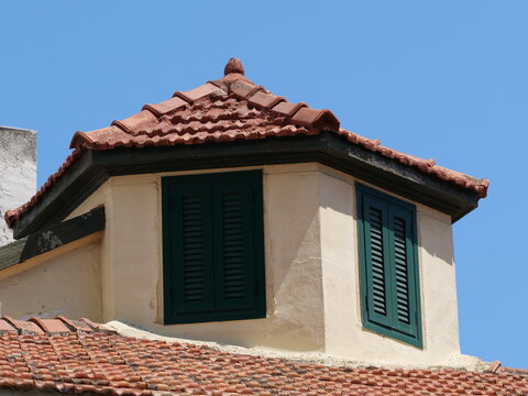 Traditional Mediterranean dormer window with green shutters and clay tiles