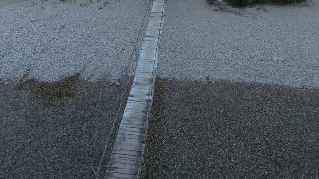 Drone Aerial View Flying Overhead Wooden Suspension Footbridge Across Pebble Riverbed in Glavaticevo
