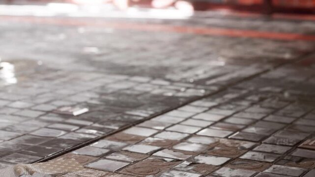 Water covers clean tiles in a busy area. The floor looks shiny as cleaning continues. The scene shows care for the environment and cleanliness. People may be nearby.