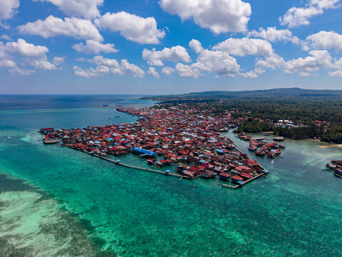 Aerial view of Mola Utara village with houses built on stilts over the turquoise sea, surrounded by clear blue water and a bright sky in South Wangi-Wangi, South East Sulawesi, Indonesia.