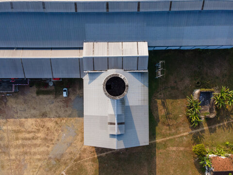 Aerial view of an industrial building with a circular chimney and metal roof, surrounded by dry grass and sparse vegetation in Banyumas Regency, Central Java, Indonesia.