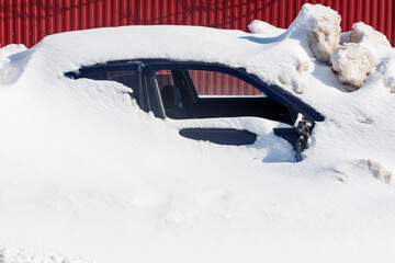 Naklejka premium Snow covers a dark car, partially buried