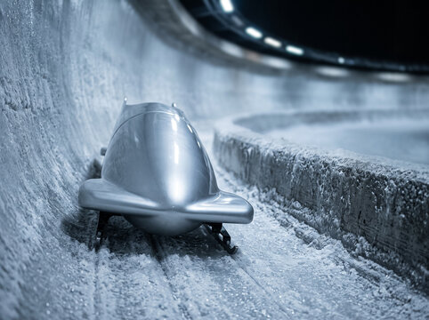 silver bobsleigh sled rushing along an icy curved track covered in snow and frost during a high-speed descent at a competition
