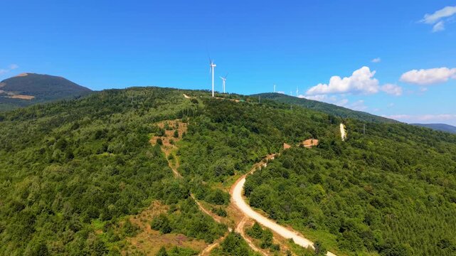 Drone Aerial View Flying Towards Wind Turbines on Mountain Ridge with Dirt Road and Forest at Ivan Sedlo