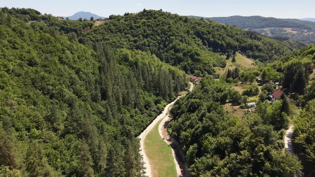 Drone Aerial View Flying Over Narrow Country Road Through Lush Green Forest and Stream Valley Near Vogosca