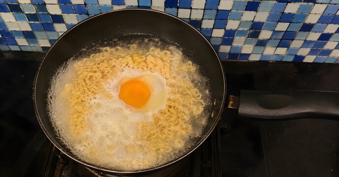 Cooking instant noodles with fried egg in boiling water, top view