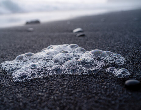 Close up of sea foam bubbling on dark volcanic sand with a shallow depth of field on a beach.