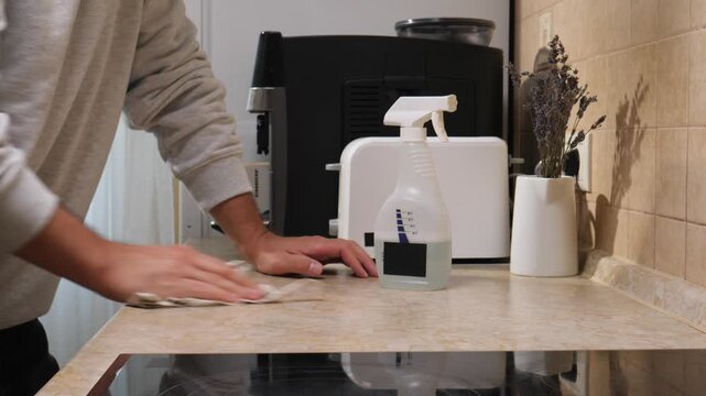 Person's hands cleaning a kitchen countertop with a reusable spray bottle and a cloth, demonstrating daily household chores and maintaining hygiene in a home environment