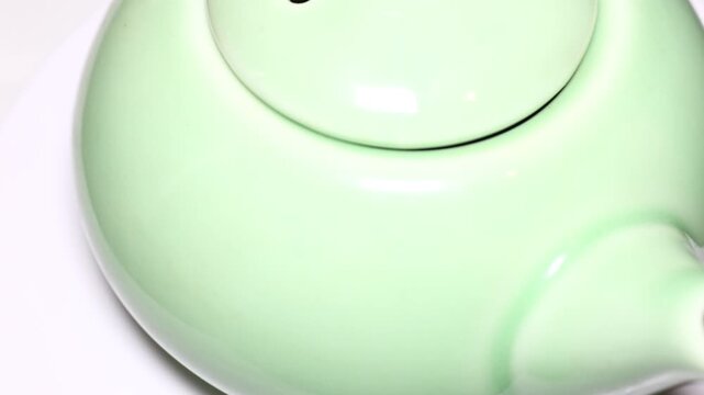 A close-up view of a green teapot sitting on a table. Rotating in a circle