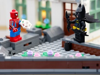 Naklejka premium Tambov, Russian Federation - August 23, 2026 Lego Spider-Man holding a web piece and Batman wielding batarangs while standing opposite each other on a brick rooftop.