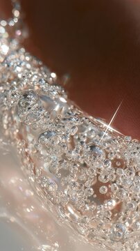 Slime with floating beads is squeezed slowly, creating a glossy and textured look in macro view under bright light.