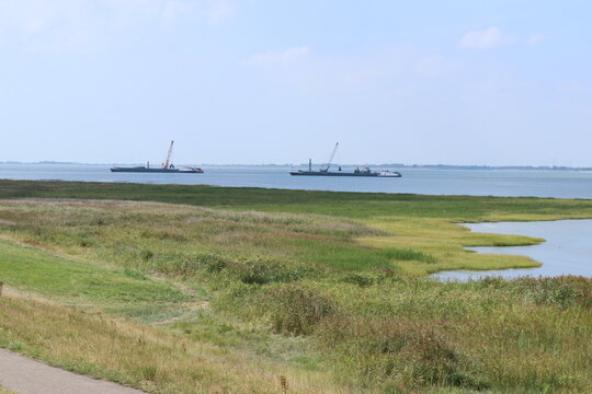 two floating cranes in the channel of the westerschelde sea for reinforcement works and a green salt marsh in front