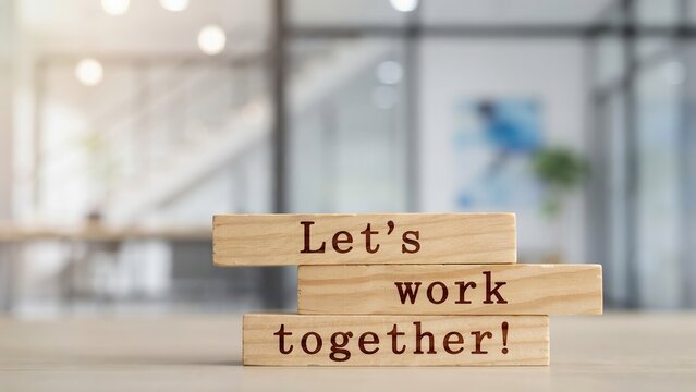 Wooden blocks stacked with the text Let's work together against a blurred office background. Professional concept for corporate collaboration and business partnership.